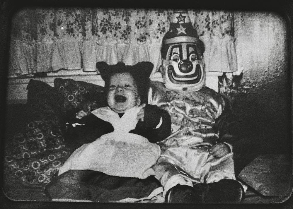 Kids in Halloween costumes. Sitting on a couch. The one on the left dressed as Aunt Jemima, which used to be acceptable. The one on the right is a clown. Black and white. 