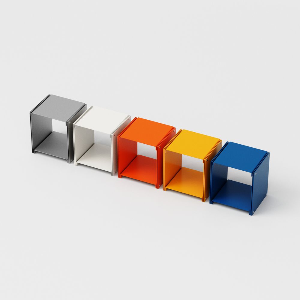 A row of five modular cube storage units in different colors: gray, white, orange, yellow, and blue. Each cube has the same minimalist design with open fronts and a shelf inside. The cubes are made of metal with visible edge detailing, showcasing a cohesive contemporary furniture collection.