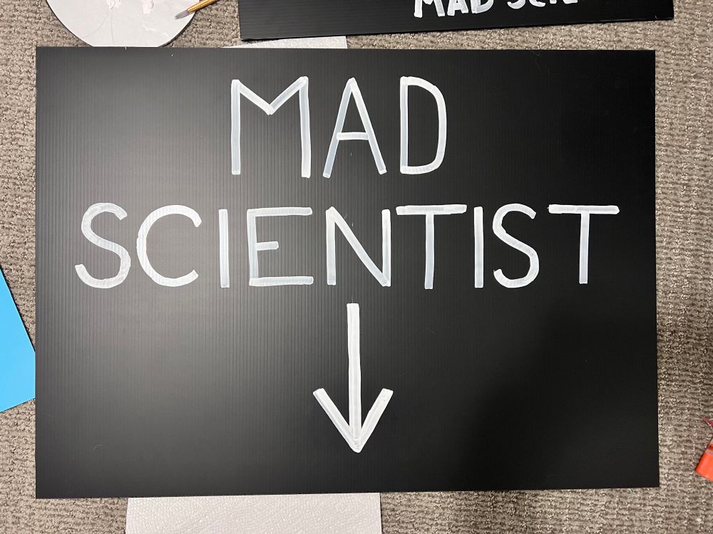Poster that reads “mad scientist” with an arrow pointing down.