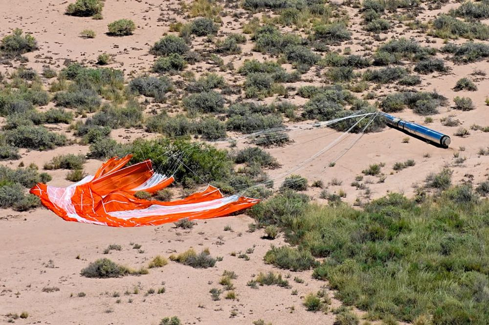 A half-ton sounding rocket payload after landing in the desert down range at White Sands Missile Range. Attached is a bright orange-red and white parachute.