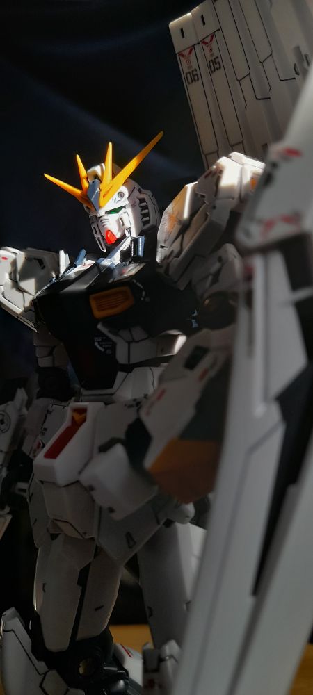 A white robot (the RG RX-93 ν Gundam) at a relaxed stance with a beam rifle and shield at its sides.