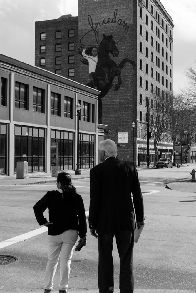 Black and white photo of two people standing in front of a building with graffiti on the side. 