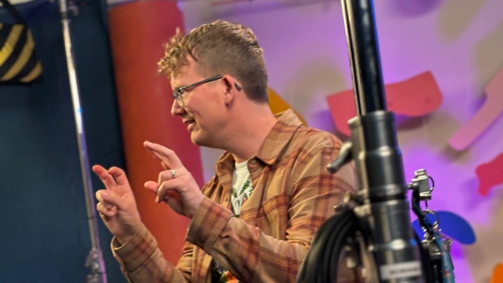 A BTS photo of Hank Green using his forefinger and middle finger on each hand out in front of him mimicking the popular US gesture to indicate sarcasm or that what you're saying is allegedly true. In this case indicating the alleged "void" 