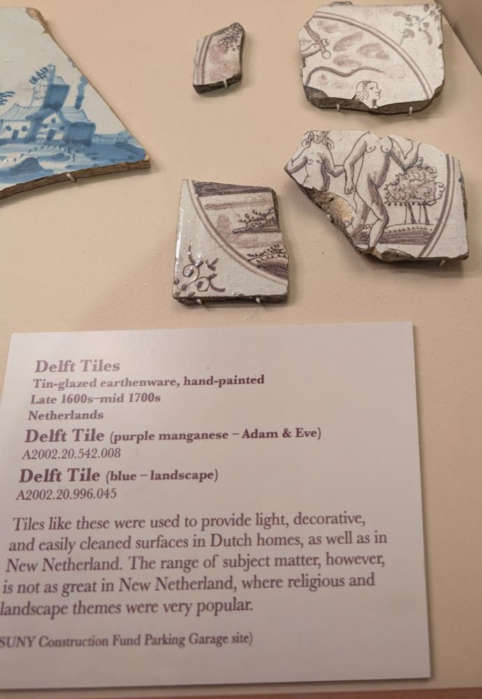 A display case of numerous deft tiles from the 1600s and 1700s. One particular one is showcasing the biblical figures Adam and Eve, both nude.