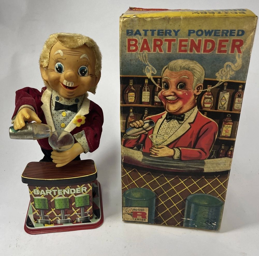 Battery-operated bartender toy next to his box. He is holding a martini glass and a shaker and smoke may come out of his ears if you believe the box. This is actually not Cragstan, but it's a knockoff of Cragstan's Charley Weaver toy.