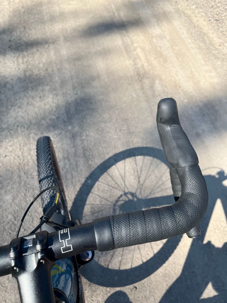 Image of the front wheel of a moving bicycle casting a shadow of the wheel onto the gravel road. 