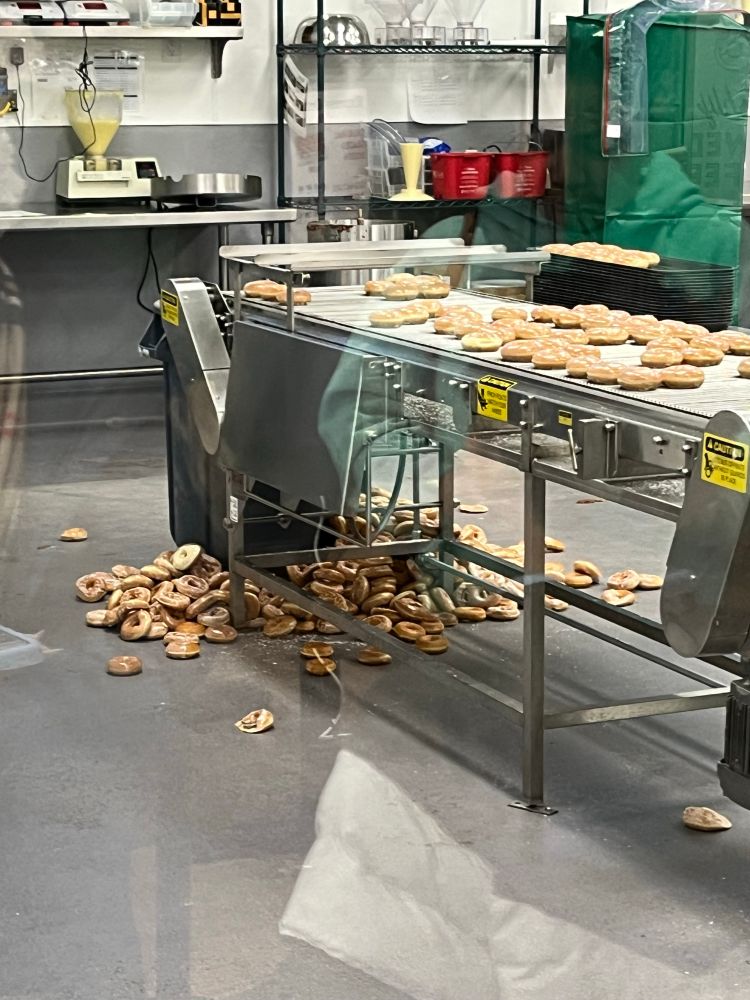 Donuts, falling off of the conveyor belt in onto the floor and a garbage can at Krispy Kreme in Fridley, Minnesota