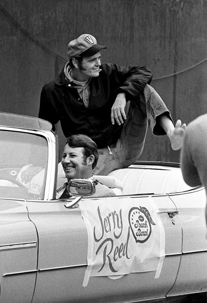 Jerry Reed rides into the 1974 Peach Bowl on the back of an open car. He is wearing a Vanderbilt baseball cap with the same V as the 2010s VandyBoys. He seems to have forgotten a shoe. 