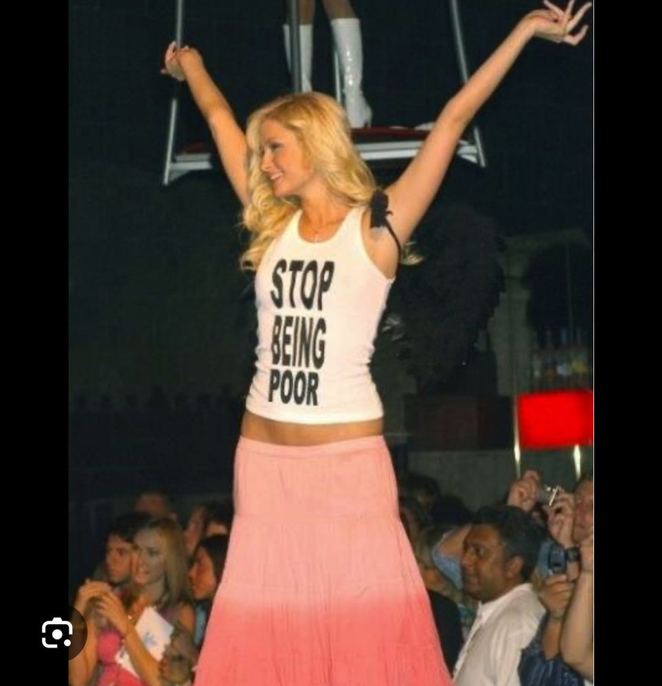 Paris Hilton se tient debout les bras levés. Elle porte un tee-shirt où il est noté « stop being poor »
