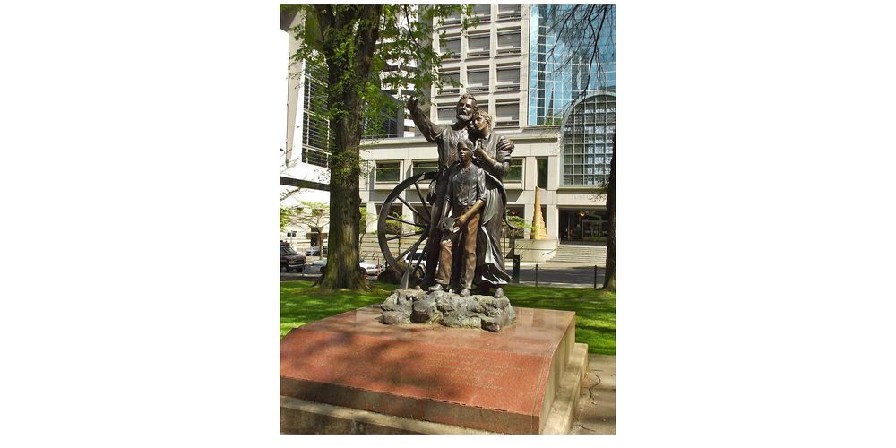 A photo of a brozened statue standing in a shaded city park.