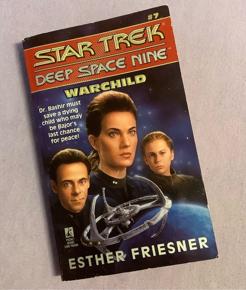 Book: Star Trek DS9. Title: Warchild. Author: Esther Friesner. Caption: Dr Bashir must save a dying child who may be Bajor’s last chance for peace! Cover: portraits of Bashir, Dax, and a Bajoran child, superimposed over the DS9, superimposed over Bajor. For some reason Dax is central and larger than Bashir.