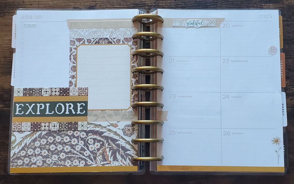a disc bound planner. the discs are large and made of gold plastic. 

the left page is a 2 panel dashboard layout with cream, brown, and gold decorations. there are some green accents. the left panel is titled "TODAY" in a green thin serif font and is a check off list. the right panel is decorated with washi tape and scrapbook paper; [from top] a ripped piece of cream washi tape, scrapbook paper with a triangular tile pattern, a lined writing areas bordered with a floral tile motif and gold foil line; the bottom is covered with a piece of cream washi tape. below the left panel and overlapping the right is a scrapbook paper piece with brown tile motifs on top and bottom, and the word "EXPLORE" on a green background with gold foil lines above and below. below both panels is a strip of scrapbook paper with brown and cream floral tile motifs that spans the width of the page. the bottom of the page is lined with gold washi tape.

the right page is an 8 box weekly layout. the first box is titled "grateful" in a green scripty font over an off cut of the triangle tile paper over a torn piece of cream washi tape. the following box is "MONDAY" which has a small pink circular Aquarius sticker; continuing thru "SUNDAY" which has a small daisy sticker. the bottom of the page is lined with gold washi tape.