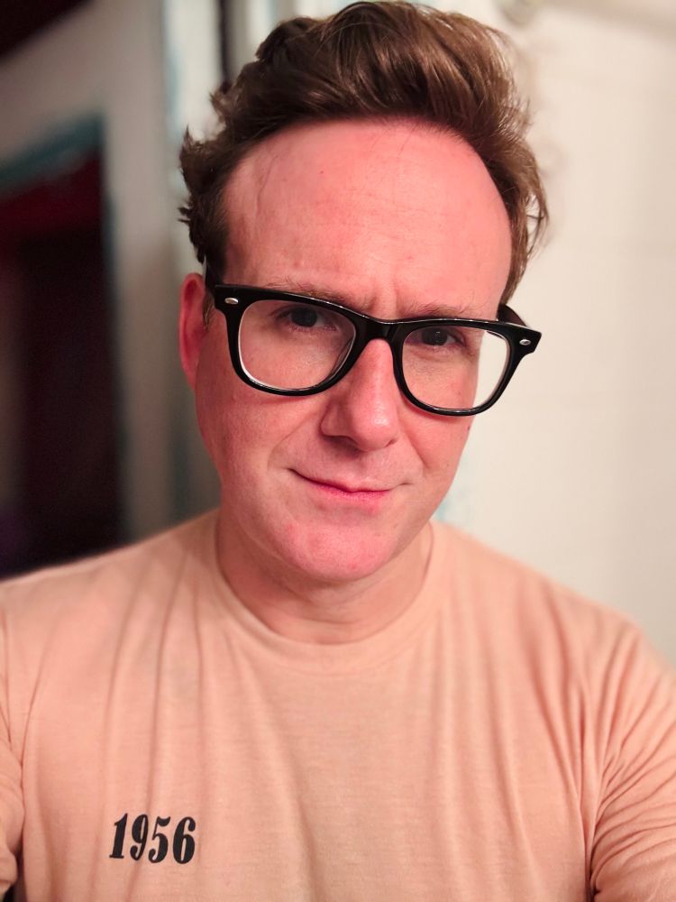 Me! White guy. Dark red hair, big hornrimmed glasses. Little smirk. Peach colored t shirt with the number 1956 on it.