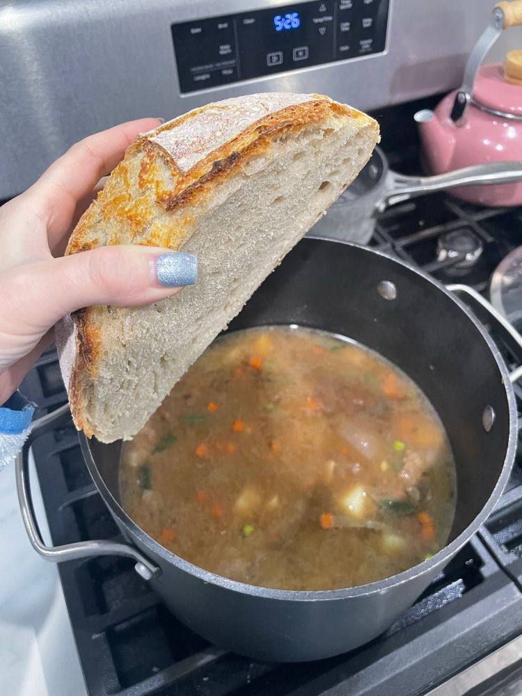 Half of sourdough bread boule and pot of homemade beef vegetable soup 