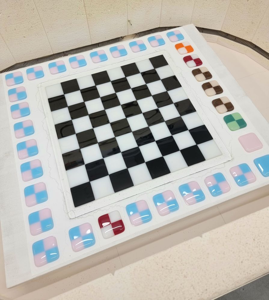 Inside a fused glass kiln showing checkered pink and blue fridge magnets and a black and white chessboard.