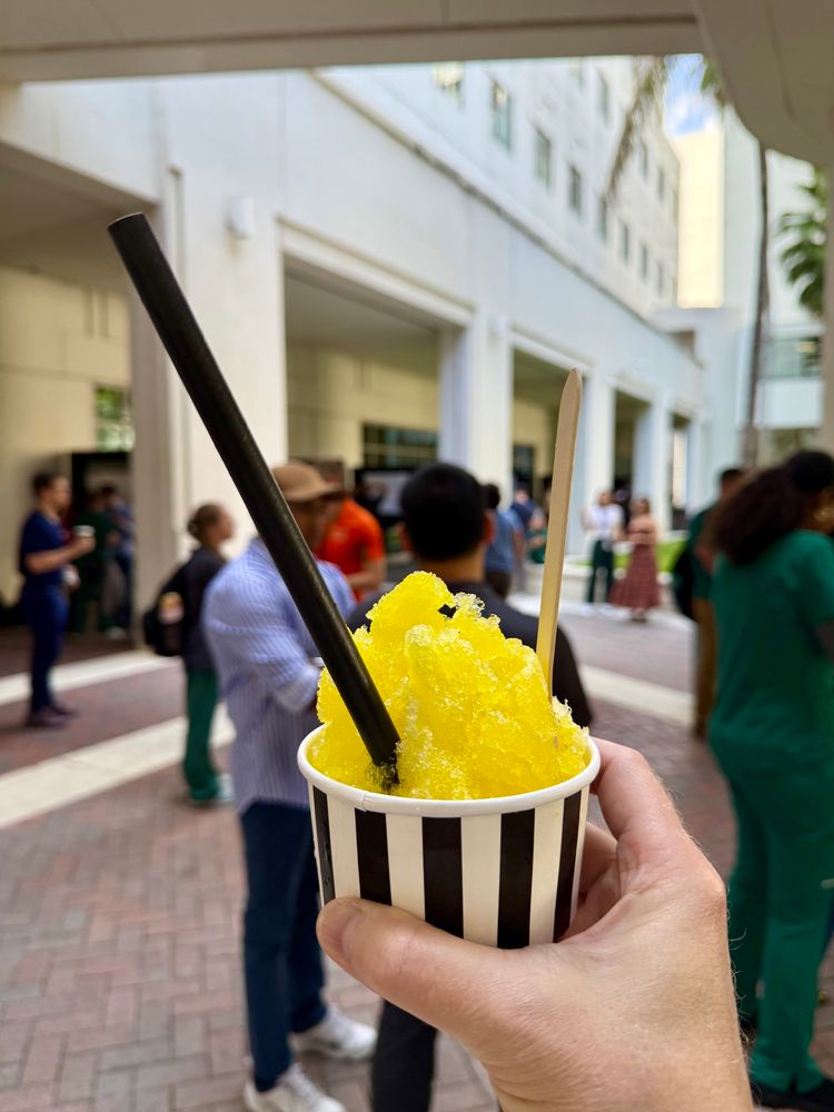 A hand is holding a cup of shaved ice with yellow flavoring (mango). 