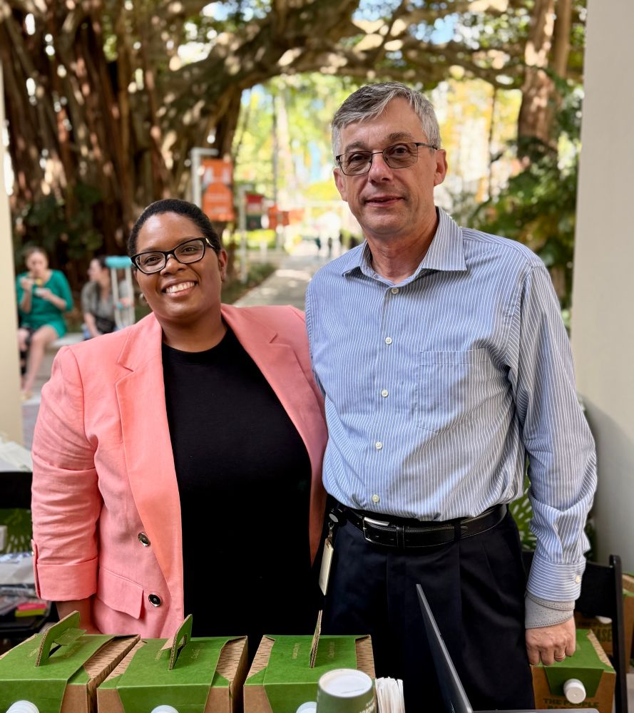 A man and a woman posing for the camera outside. There are boxes of coffee in front of them. 