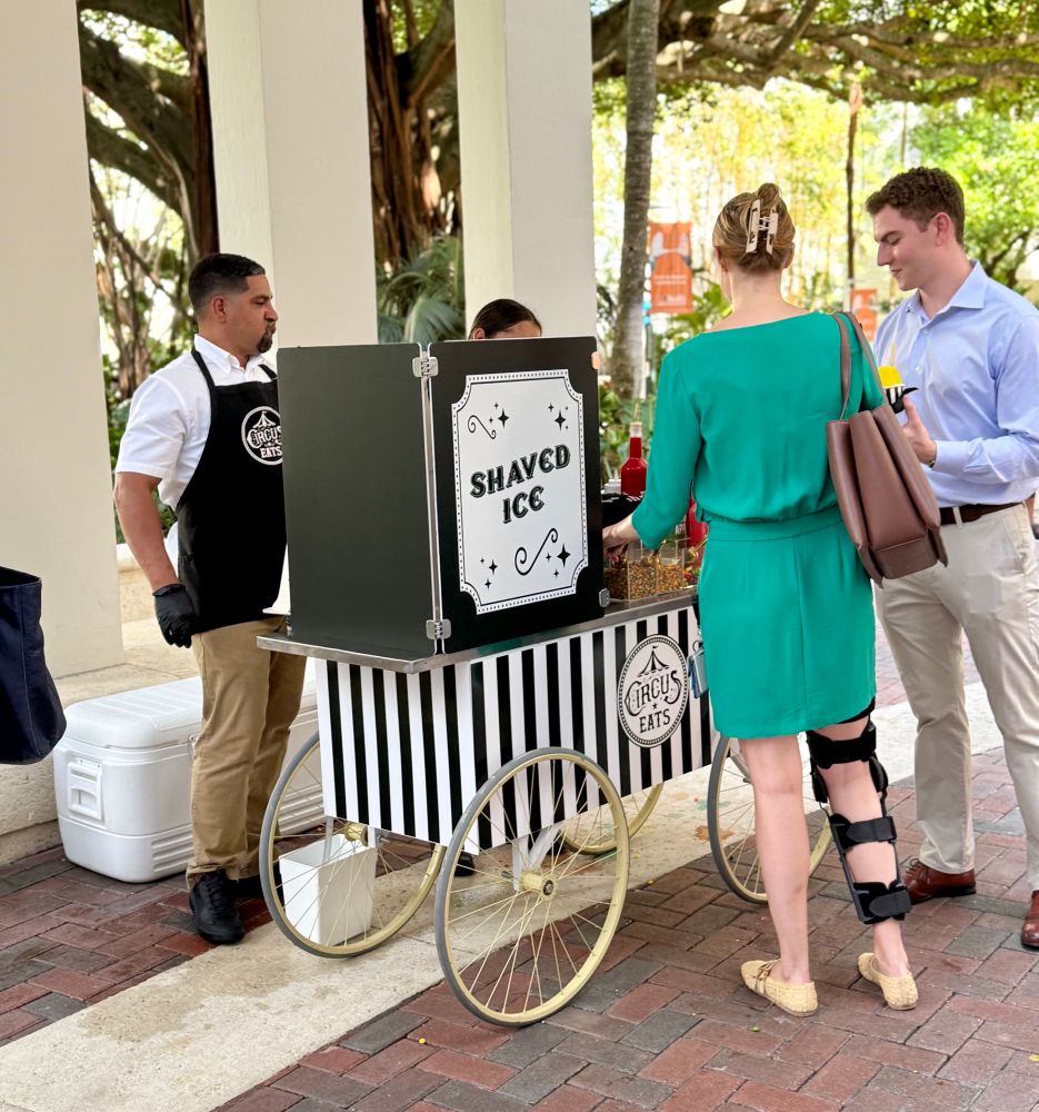 People stand in front of a food truck selling shaved ice. 