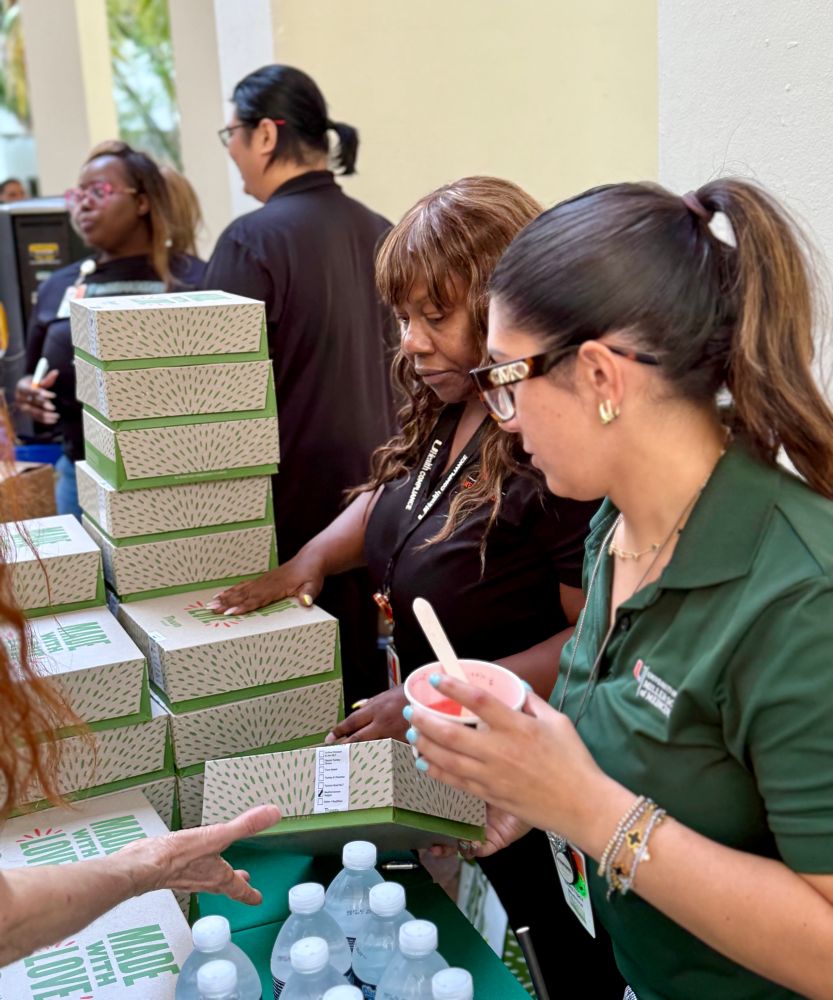 Two women are handing out box lunches. One of the women has an Italian ice up in her hand. 