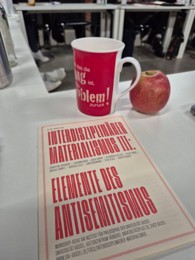 Foto vom Flyer des Workshops "Interdiszipliner Materialismus 3: Elemente des Antisemitismus" an der Universität Kassel, neben Kaffeetasse und Apfel