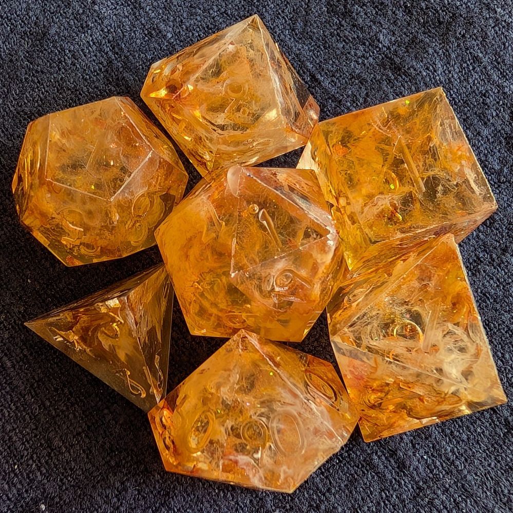 It's the cap/mold seam faces on a polyhedral set of seven dice used for playing ttrpg games like DND. Orange, yellow, amber, and white ink tendrils dance together in these translucent dice. Orange to green tone shimmer.