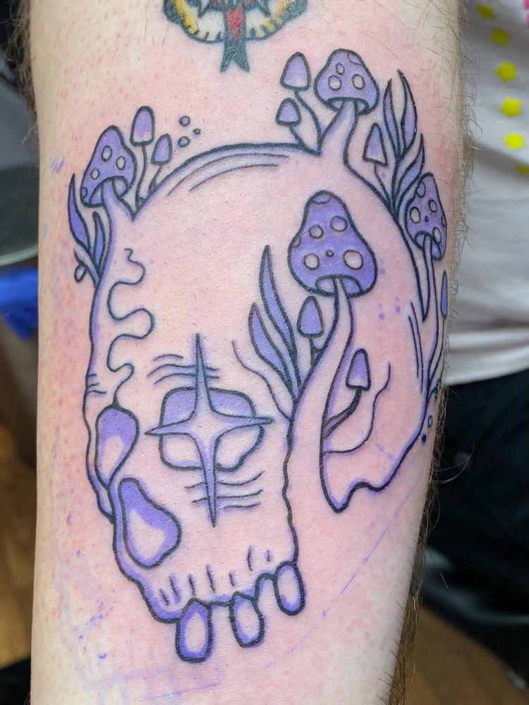 a black outline tattoo of a decomposing skull and mushrooms