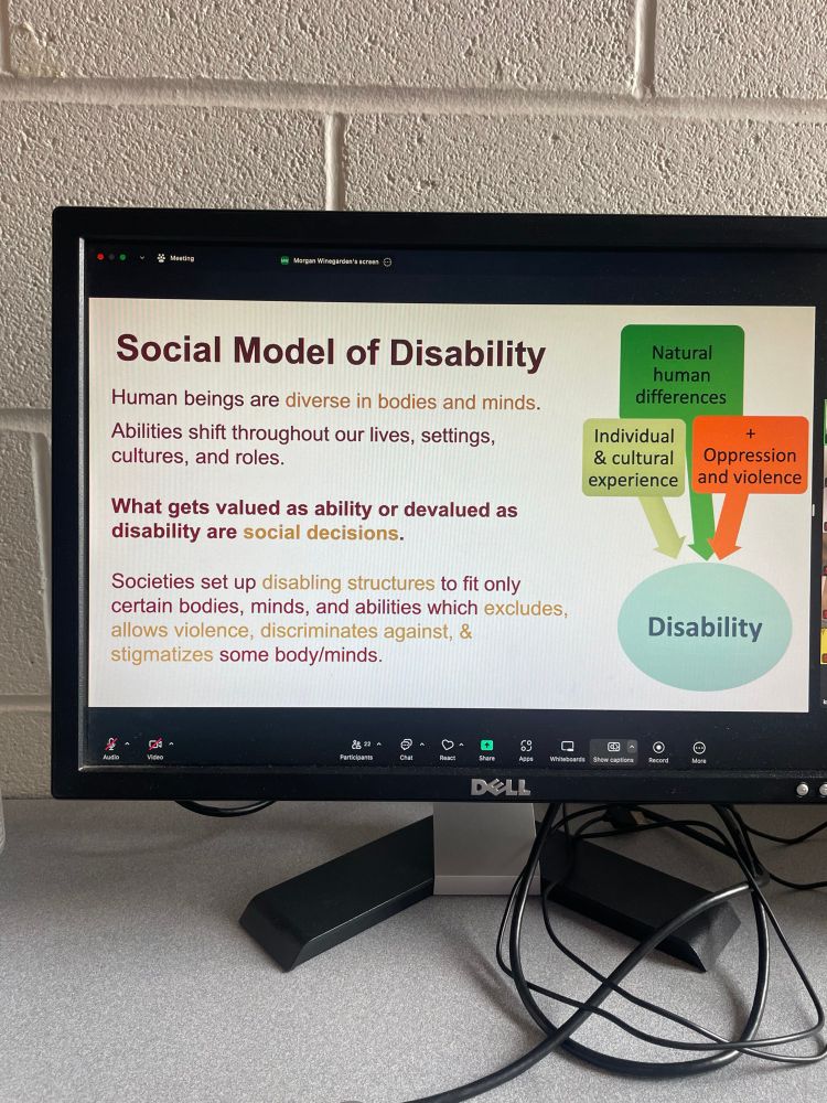 Photo of a slideshow on a computer screen, which says in maroon and gold text: “Social model of disability: human beings are diverse in bodies and minds. Abilities shift throughout our lives, settings, cultures, and roles. What gets valued as ability or devalued as disability are social decisions. Societies set up disabling structures to fit only certain bodies, minds, and abilities which excludes, allows violence, discriminated against, and stigmatizes some body/minds.” A graph draws arrows from boxes listing “individual and cultural experience,” “natural human differences,” and “oppression and violence” down to “disability”