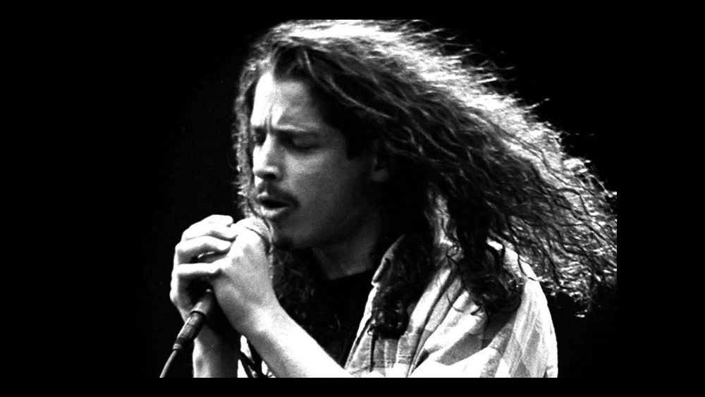 Black and white photo of Soundgarden and Audioslave frontman Chris Cornell in one of his long haired eras singing into a mic 