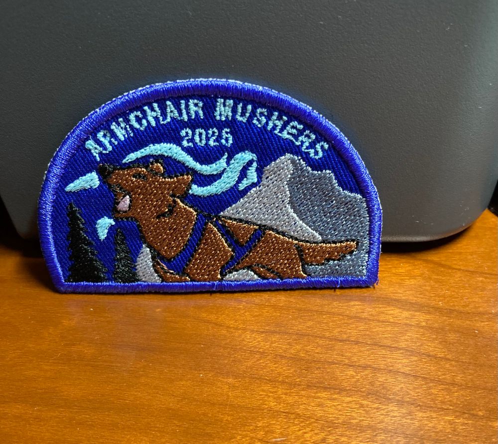 Hand-sewn patch in blue and tan with a brown sled dog. It says: Armchair Mushers 2025