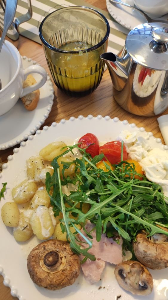 Une assiette avec des gnocchis, des tomates cerises, des champignons, de la salade roquette et du jambon