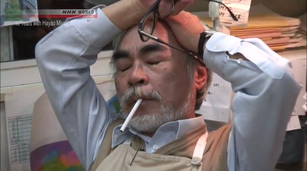 Hayao Miyazaki, stroking his head, glasses off, cigarette in his mouth, looking entirely done with everything.
