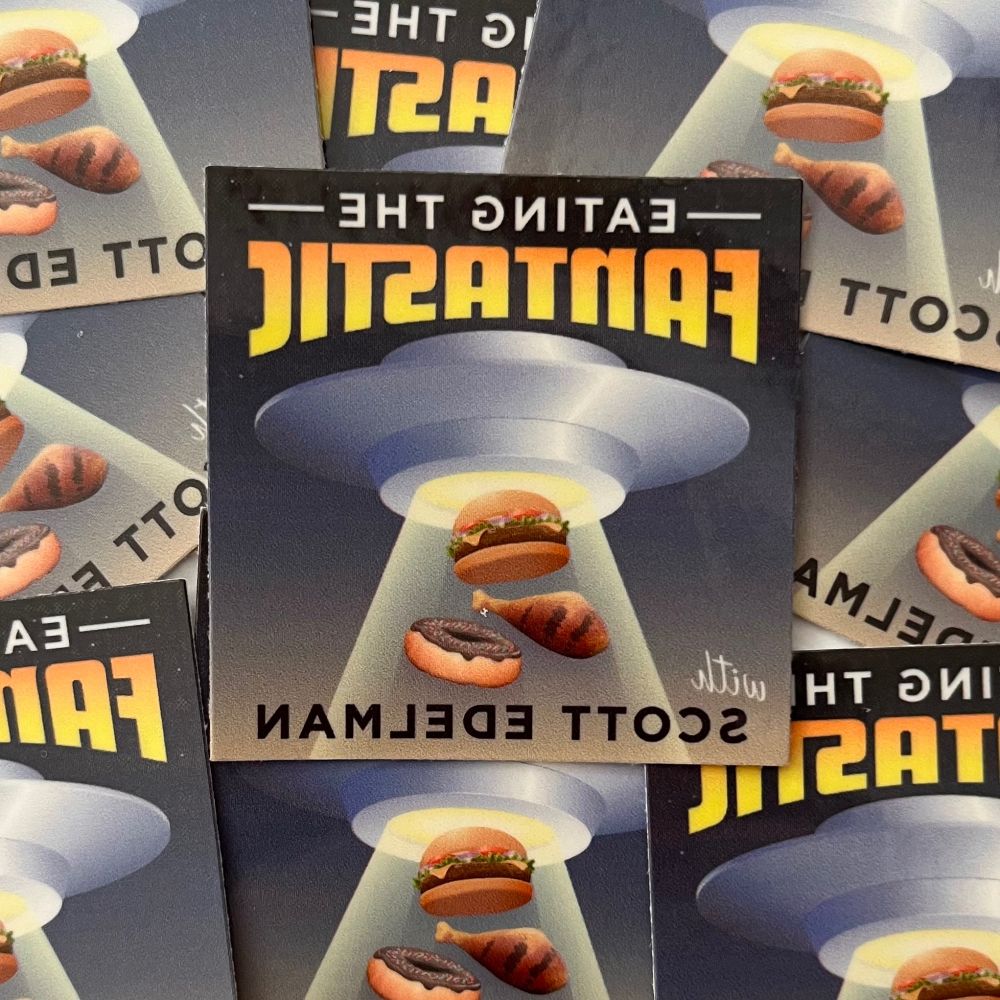 The Eating the Fantastic icon, showing a flying saucer using its tractor beam to lift a hamburger, chicken leg, and donut. Only it's backward, with the words EATING THE FANTASTIC and WITH SCOTT EDELMAN printed in reverse.