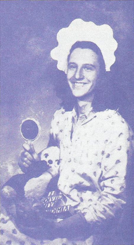 Photograph of a grown man wearing baby clothes, and holding a rattle, alphabet blocks, and a stuffed animal.