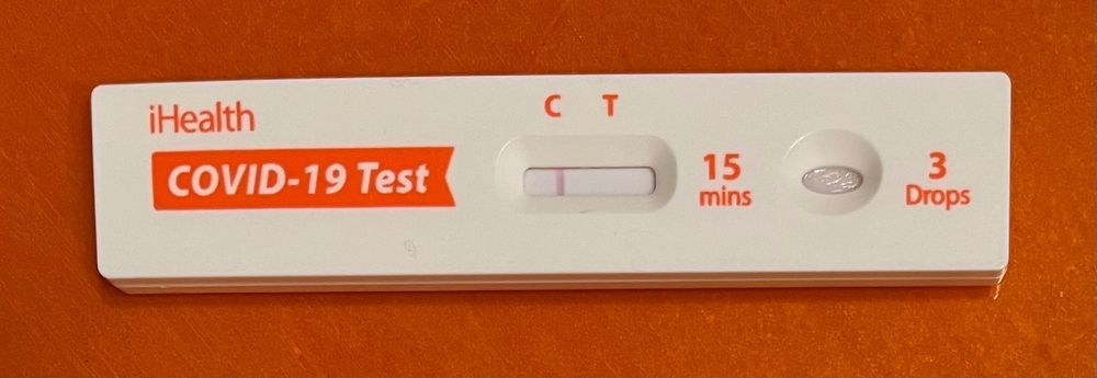 A COVID-19 test with a negative result, photographed against an orange background.