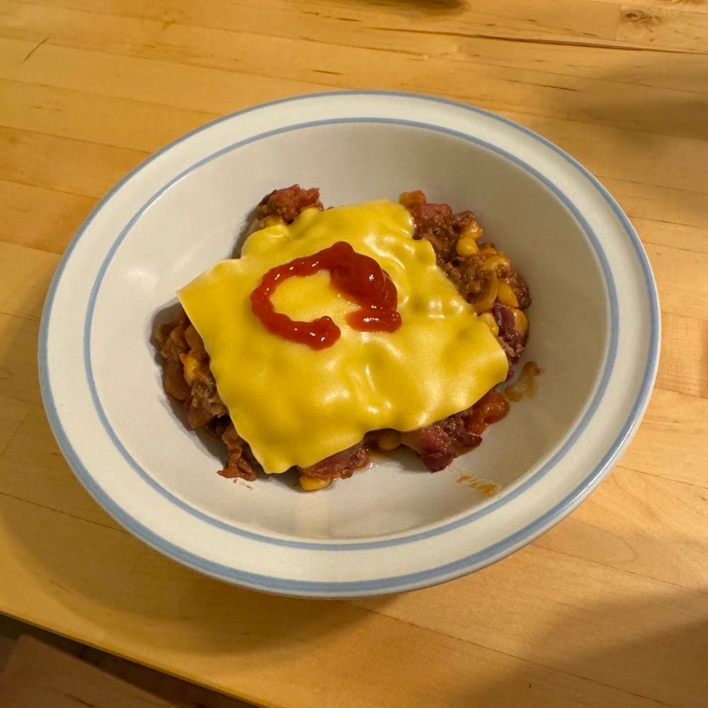 A bowl of chili including smashed patty pieces, beef fat fried onions, Illinois sweet corn, topped with American cheese and ketchup 