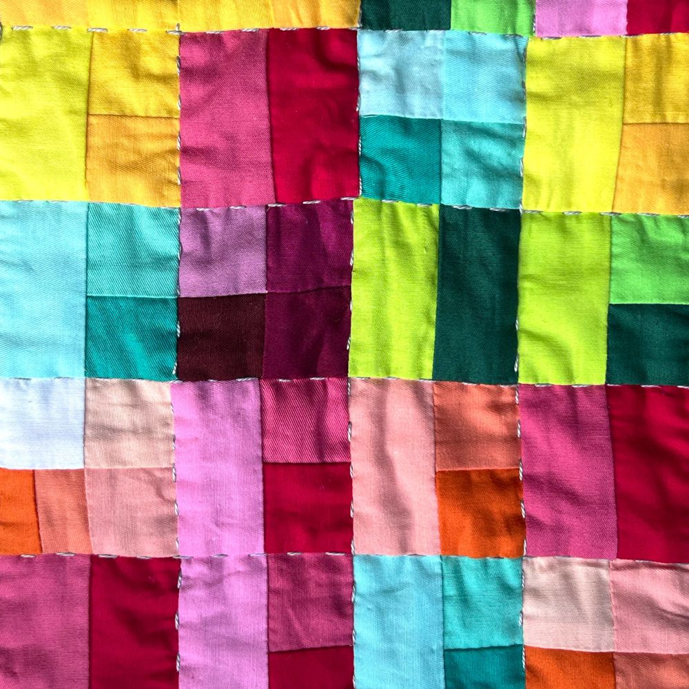 A close up of the quilt with multi colored blocks, crinkly fabric, and gray stitches separating the blocks.