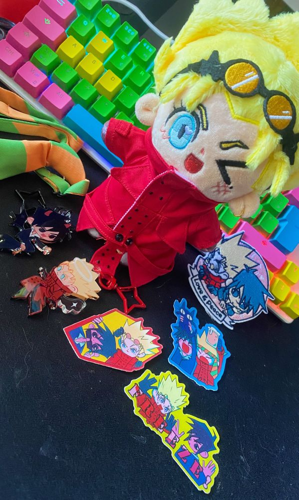 98’ Vash-plush by Kreamroll surrounded by extras he came with: Wolfwood & Vash charms, stickers and fabric patch. Also a small tie to go around his head. 