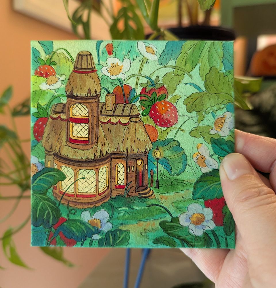 Hand holding small painting on watercolor panel featuring a thatched roof bakery and strawberries 
