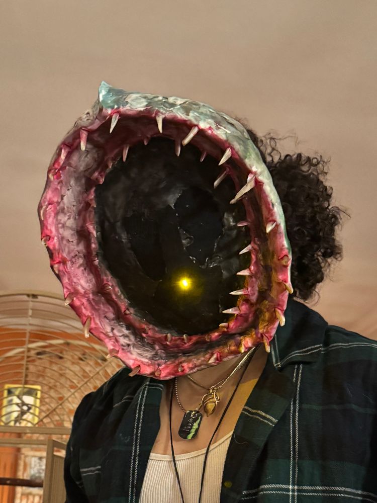 A teenager in flannels wearing a mask that looks loke the gaping toothy maw of a giant leech