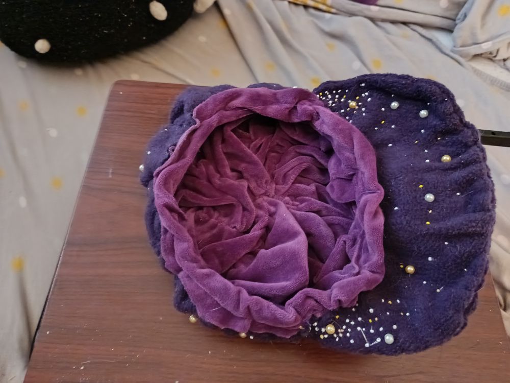 Une casquette gavroche violet foncé avec des perles plus ou moins grosses allant du blanc au doré, du jaune à l'argenté. Vue de dessus et à l'envers : on voit le fond violet clair de la casquette 