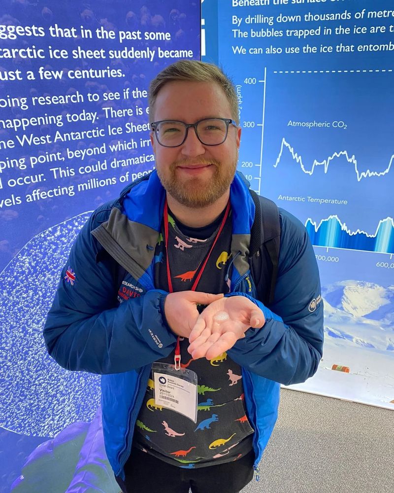 Dylan holding a small piece of melting ice core from Antarctica while stood in front of display boards with information about Antarctica on them