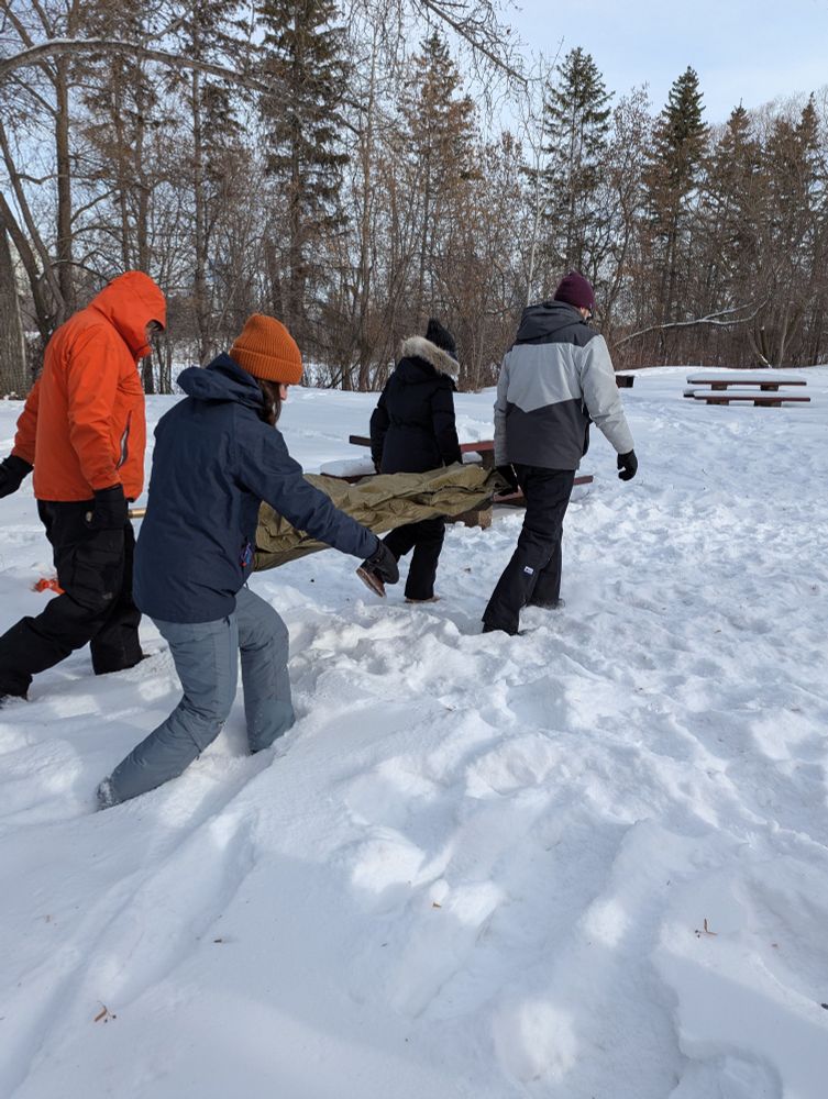 Four people carrying a mannequin casualty on a stretcher through the snow.