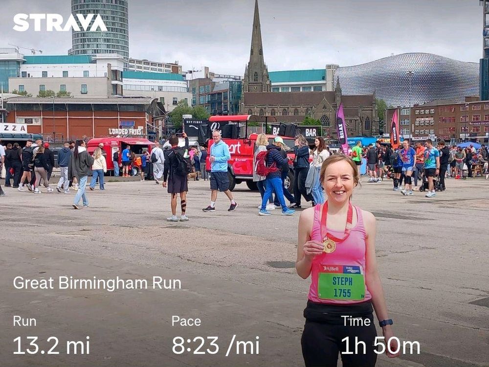 Person holding medal in front of Birmingham skyline showing Rotunda and Selfridges. Distance 13.2 miles, Pace 8:23/mile, Time 1:50:21 