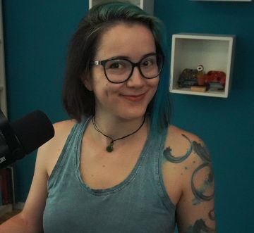 2DKiri sitting at her desk in her studio smiling. She's wearing a blue tank top and a jade necklace.