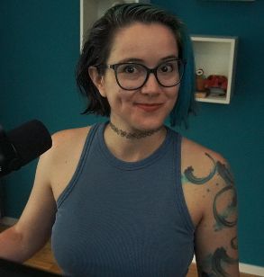2DKiri sitting at her desk in her studio smiling. She's wearing a blue tank top.