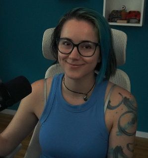 2DKiri sitting at her desk in her studio smiling. She's wearing a blue tank top and a jade necklace.