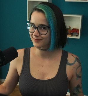 2DKiri sitting at her desk in her studio smiling. She's wearing a grey tank top.