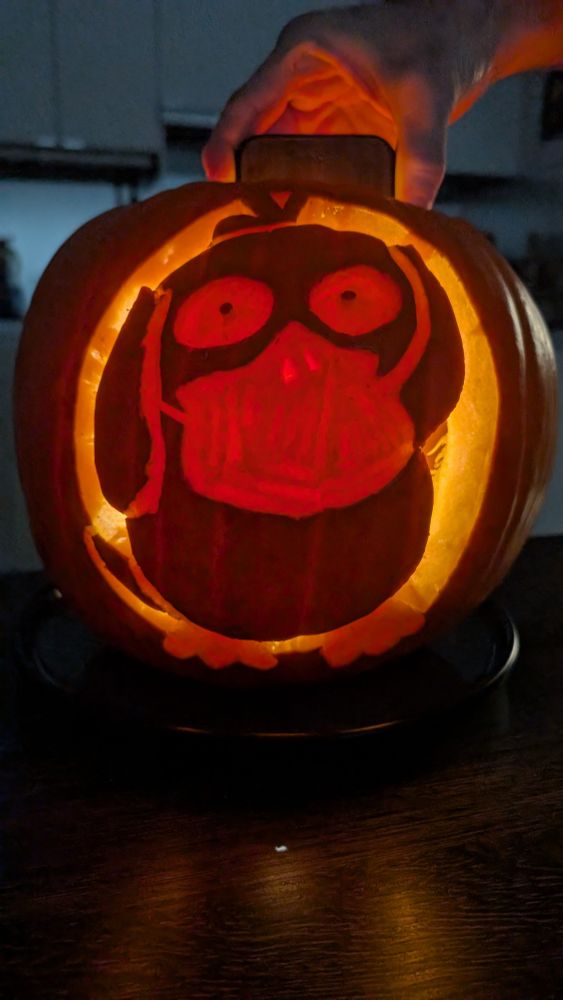 Psyduck Pokémon carved into a pumpkin. A hand is holding a phone with a torch inside to light it.