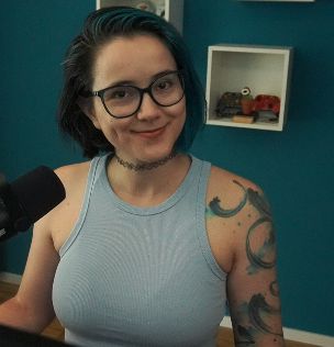 2DKiri sitting at her desk in her studio smiling. She's wearing a blue tank top.