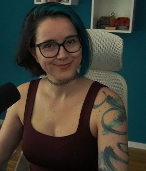 2DKiri sitting at her desk in her studio smiling. She's wearing a maroon tank top.